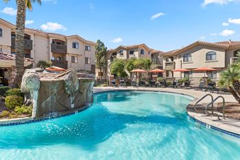 A swimming pool with a waterfall feature in front of apartment buildings.